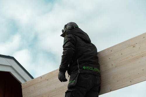 Isolerab-medarbetare bär träskiva upp till vindsutrymme i samband med isoleringsarbete på villa