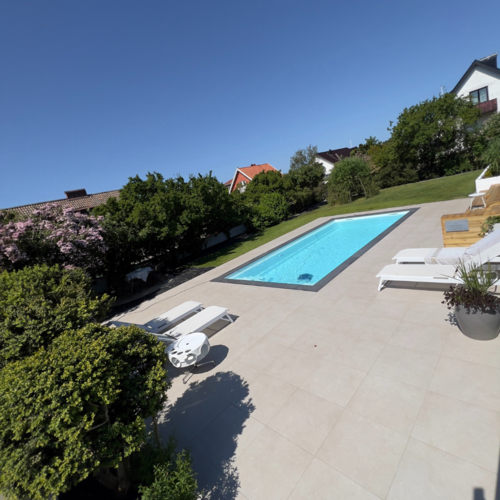 Karlssons Stensättning har skapat en elegant uteplats med beige plattsättning och pool omgiven av lummig trädgård