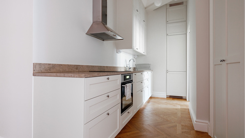 Vitt kök med rostfri fläkt, inbyggd ugn och fiskbensparkett i Vasastan, renoverat av Jobryan Bygg i Stockholm