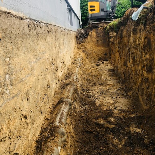 Djup dräneringsschakt med synliga dräneringsrör och grävmaskin i bakgrunden