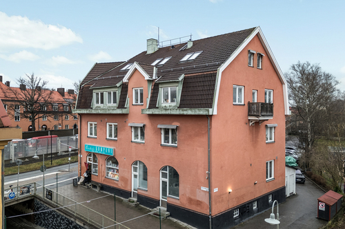 Rosa flerfamiljshus med butik i bottenplan och sadeltak, fotat från gatan