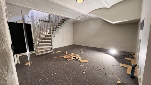 Källarlokal med rivningsmaterial på golvet och trappa mot övervåning