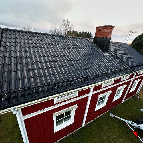 Rött trähus med vitmålade detaljer och nylagt svart plåttak fotograferat från ovan.