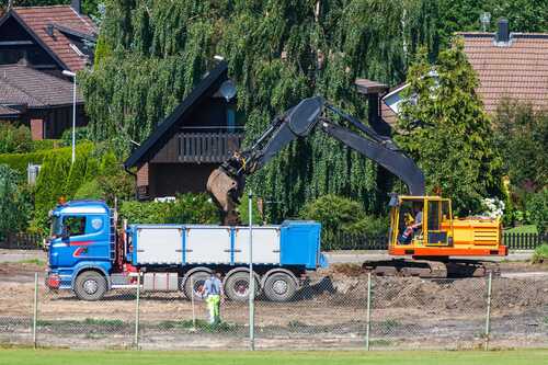 Grävmaskin lastar jord på tippbil i villaområde