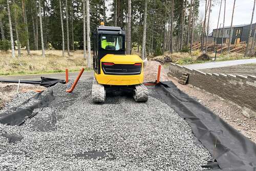 Bandgrävare på nylagd grusbädd i skogsmiljö
