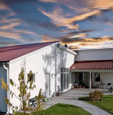 Vitt hus med rött plåttak i solnedgång – energieffektiv taklösning av Takgruppen Sverige AB.