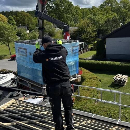 Medarbetare från Takgruppen Sverige AB tar emot leverans av takpannor via kran på byggarbetsplats.