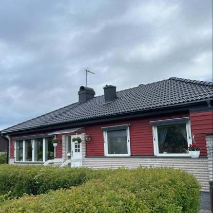 Enplansvilla med svart tak och röda fasadpaneler – takarbete utfört av Takgruppen Sverige AB.