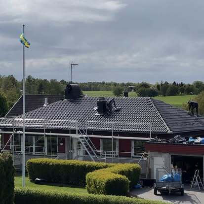 Takläggare från Takgruppen Sverige AB arbetar på svart tak med byggställning och svensk flagga i bakgrunden.