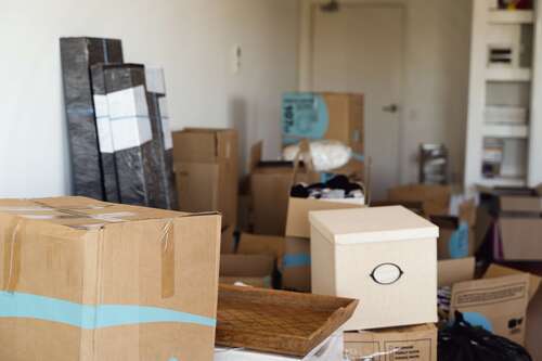 Flera flyttkartonger och inplastade möbler i ett hem under flytt.