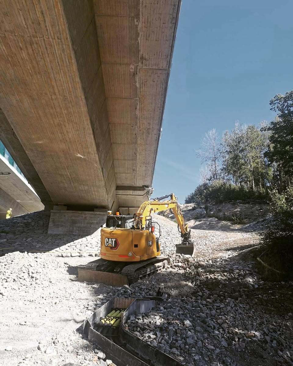 Grävmaskin i arbete under bro – avancerat schakt- och anläggningsarbete i Stockholm