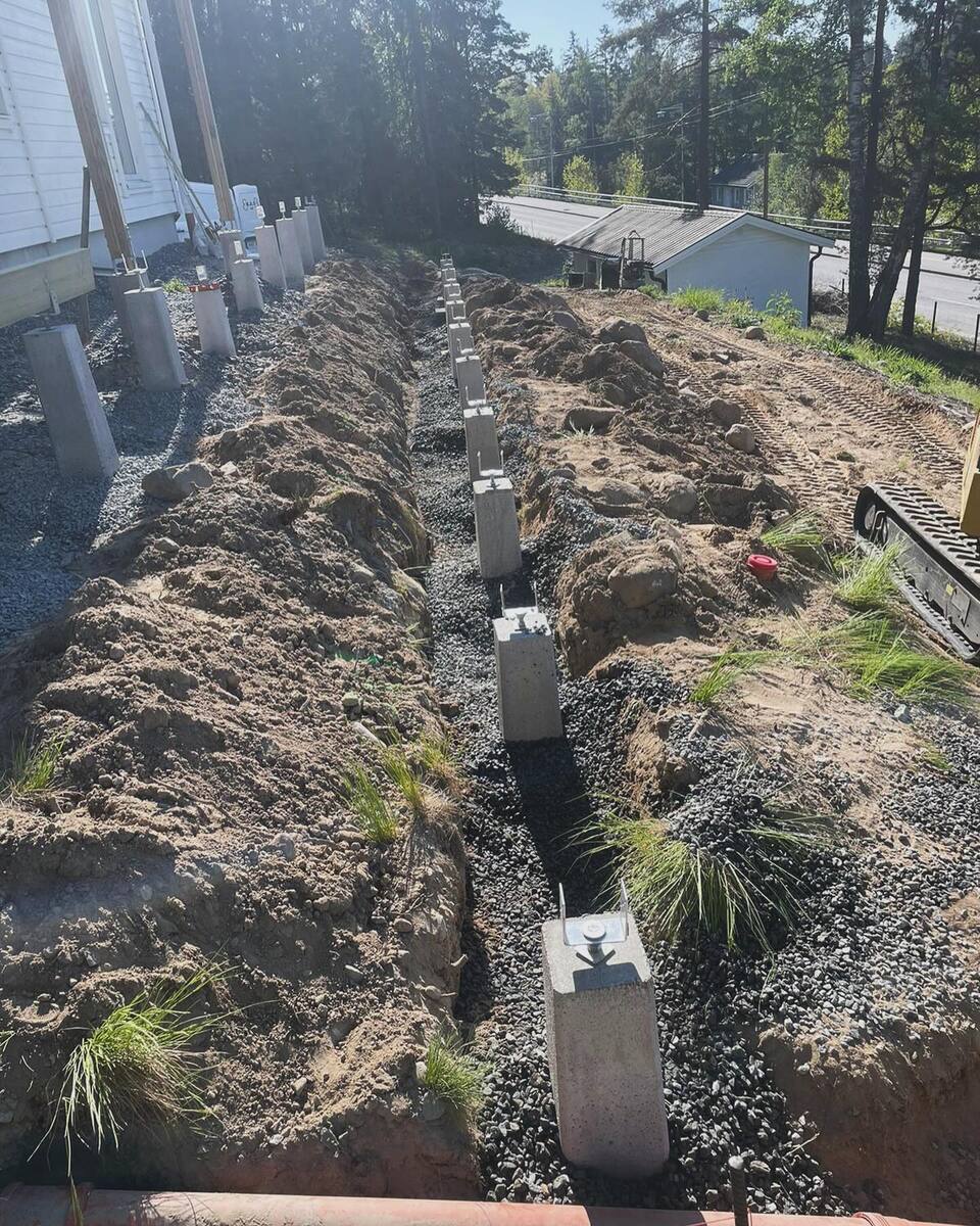 Grundarbete med betongplintar för altanbygge vid vit villa – plintgrundläggning i kuperad terräng