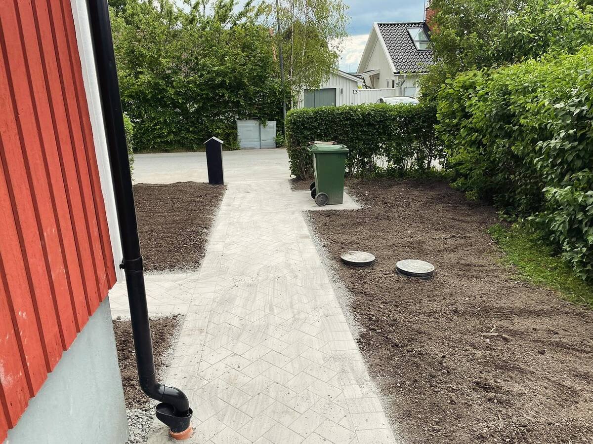 Stensatt gångstig intill röd villa med färdigställd matjord – anläggning av entré och trädgårdsgång