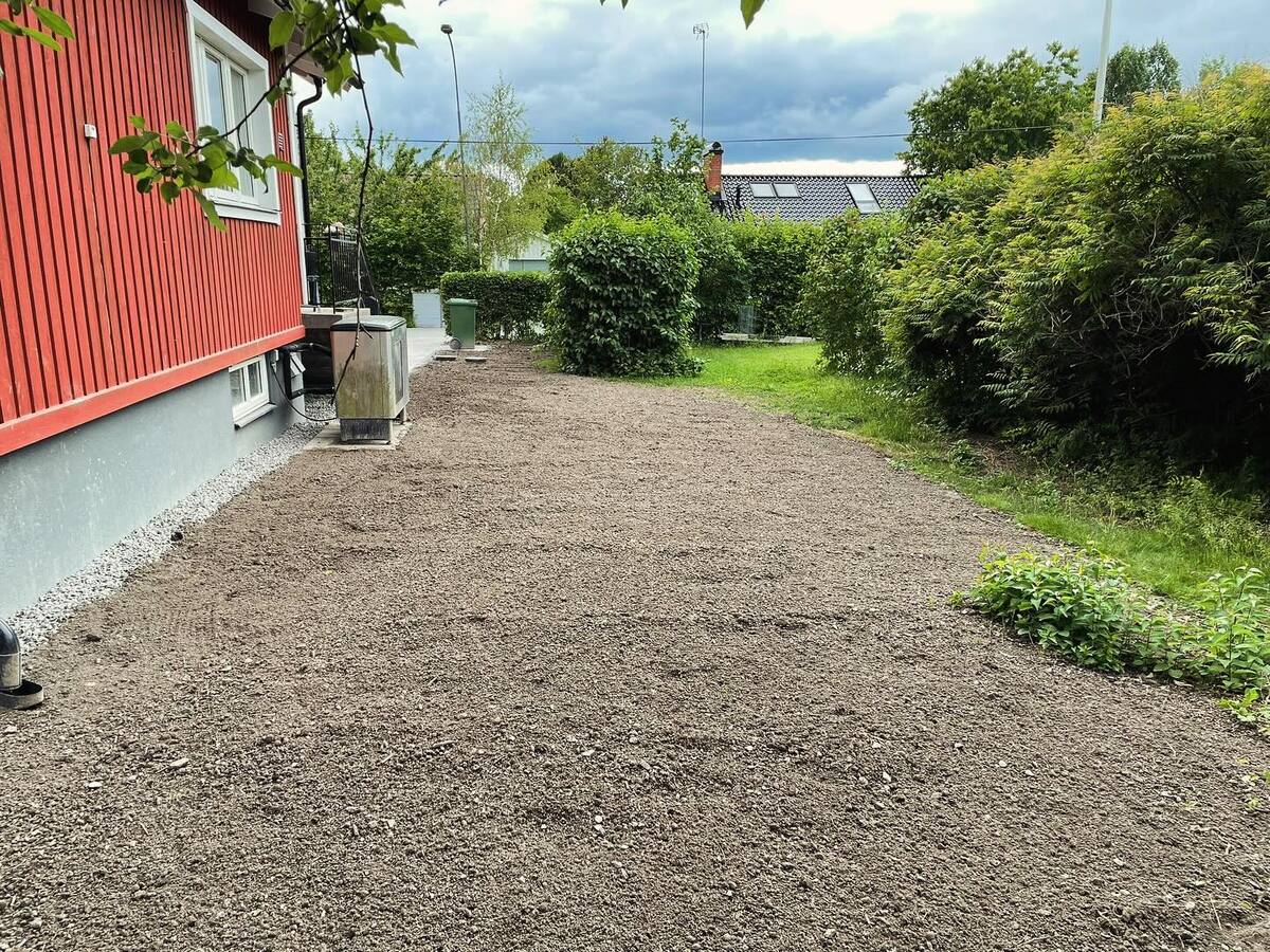 Nyplanerad trädgård med utjämnad matjord intill röd villa – förberedelse för grässådd i Täby