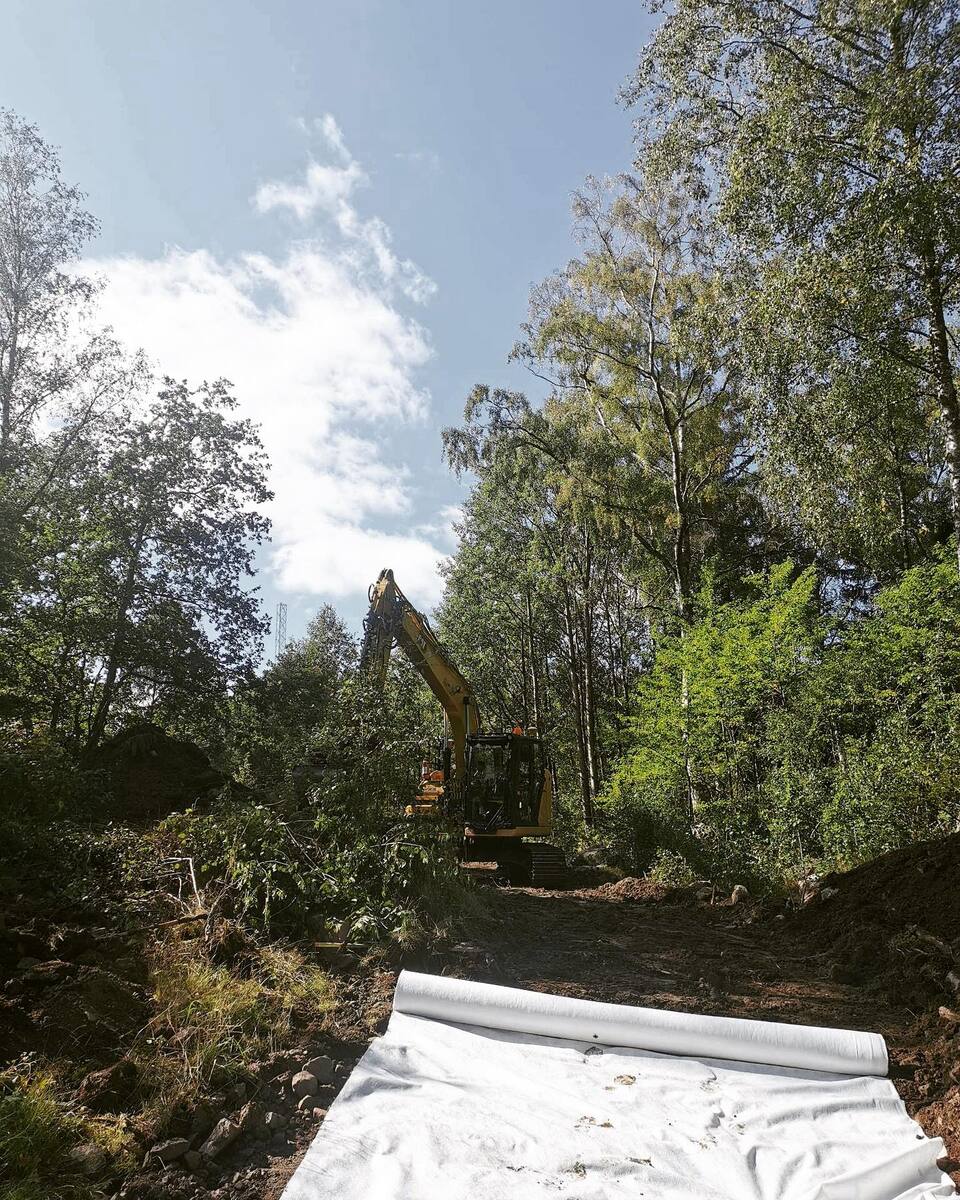 Schaktning i skogsmiljö med markduk i förgrunden – vägförberedelse med grävmaskin i Roslagen