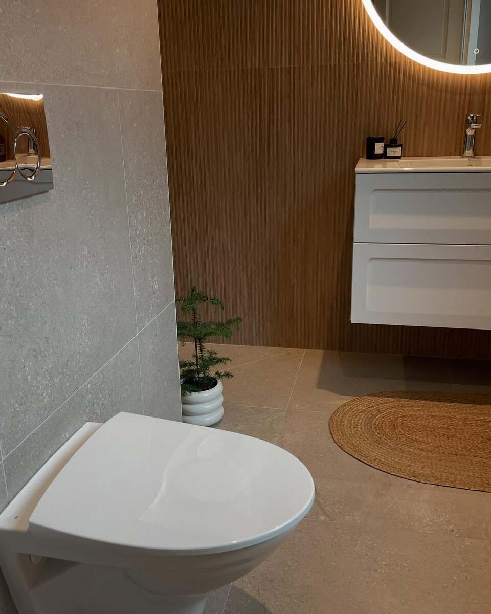Ljust badrum i Gävle med vägghängd WC, trädetaljer och spegel med LED-belysning – stilren installation av LA Rörsystem AB.