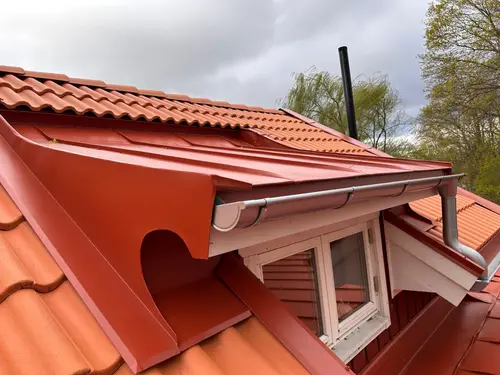 Rött plåttak med takpannemönster och specialbyggd plåtdetalj vid fönster