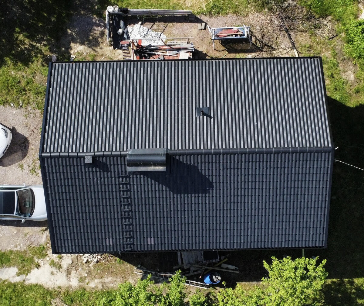 Flygfoto över hus med svart tak i plåt med takpannemönster