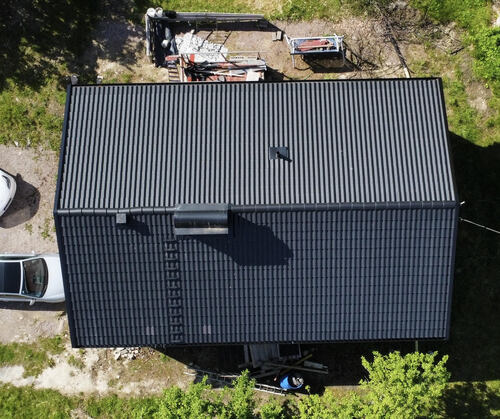 Flygfoto över hus med svart tak i plåt med takpannemönster