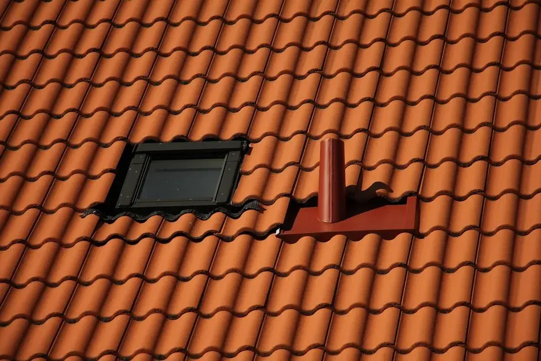 Närbild på tegeltak med takfönster och ventilationshuv i röd plåt monterat på sadeltak.