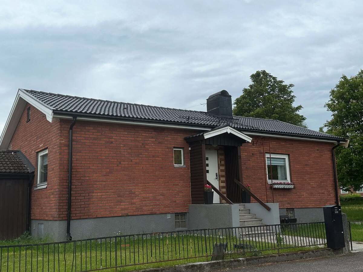 Röd tegelvilla med nylagt svart tak och centralt placerad skorsten, omgiven av gräsmatta och staket.