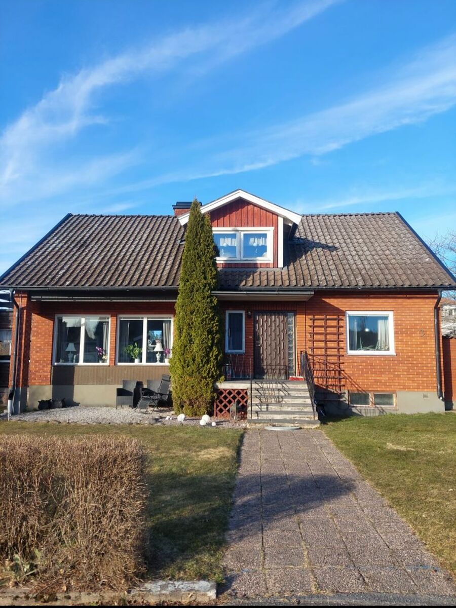 Tvåplansvilla i tegel med svart tak och frontespis, fotograferad från infart en solig dag i Örebro.