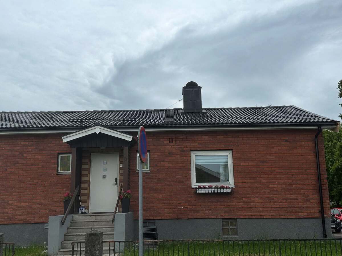 Tegelfasad på klassisk enplansvilla med nylagt svart tak och centralt placerad skorsten i Örebro.