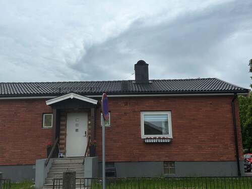 Tegelfasad på klassisk enplansvilla med nylagt svart tak och centralt placerad skorsten i Örebro.