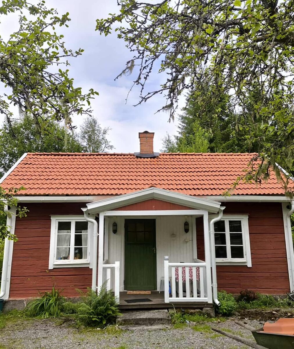 Röd träfasad på äldre villa med nytt tegeltak och vit veranda, omgiven av grönska i Örebro.