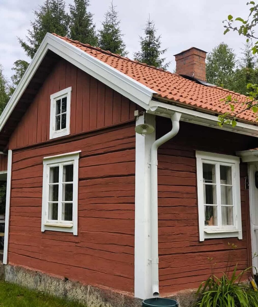 Gavelvy av röd villa med vitmålade fönster och nytt tegeltak i lantlig miljö.