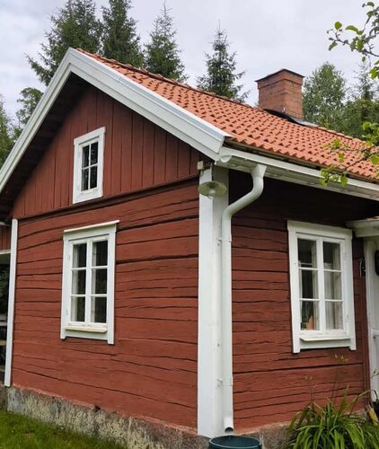 Gavelvy av röd villa med vitmålade fönster och nytt tegeltak i lantlig miljö.