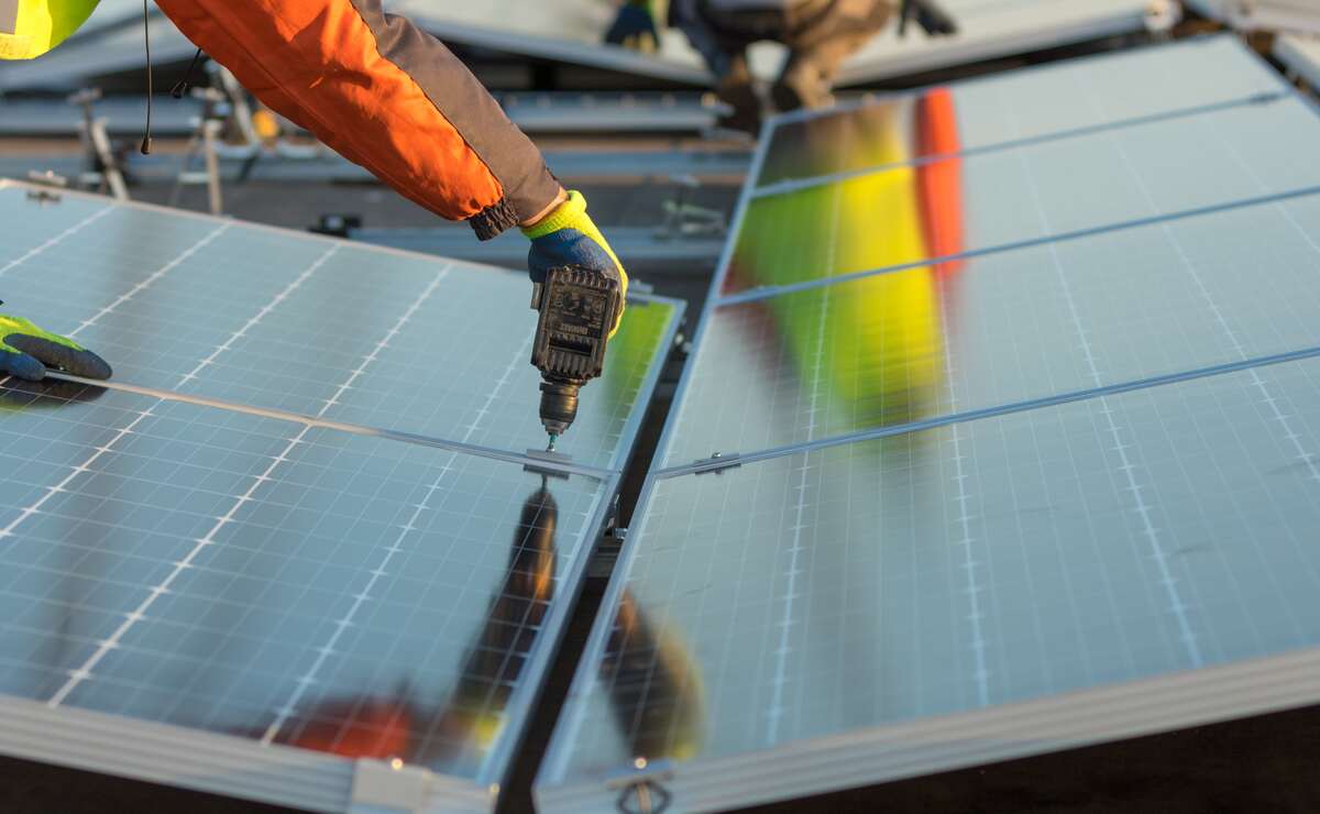 Montör installerar solpaneler på ett tak i Örebro med hjälp av borrmaskin – del av pågående solcellsanläggning.