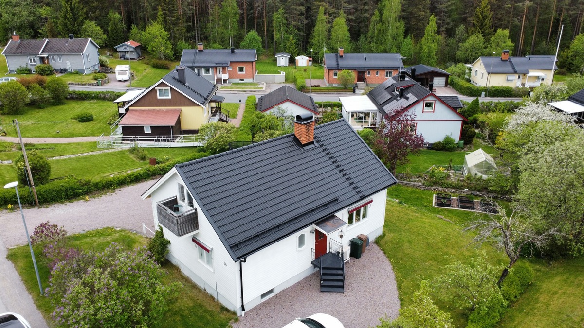 Flygfoto över villa med svart tak i takpannemönster och inglasad altan