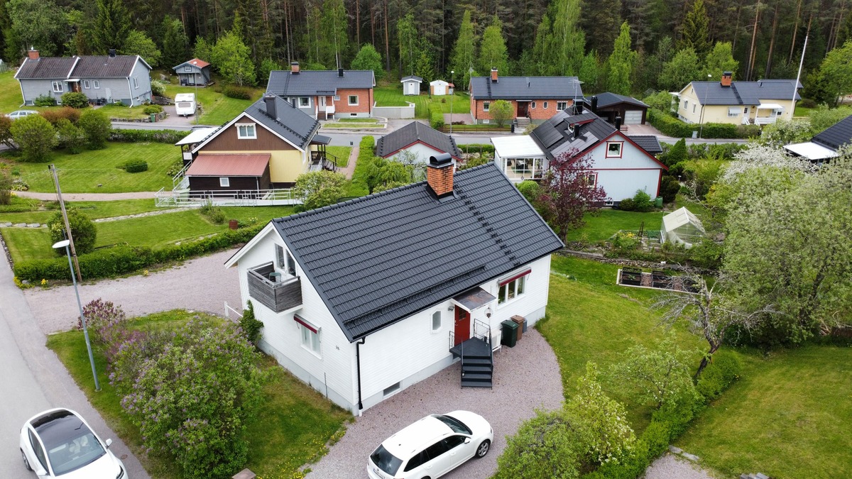 Flygfoto över vit villa med nytt svart tak i takpannemönster i villaområde