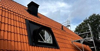 Ett rött tegeltak med takfönster och svart plåtdetalj.
