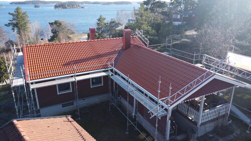 Ett rött hus med rött tak och byggställningar vid havet.