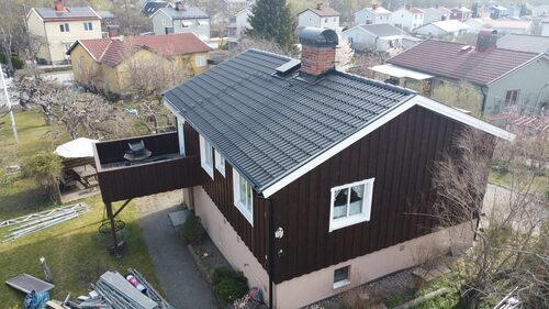 Ett mörkbrunt hus med nylagt svart tak, fotograferat från ovan.