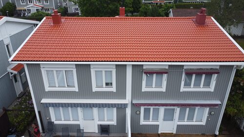 Grått tvåplanshus med nytt rött tegeltak och två skorstenar.
