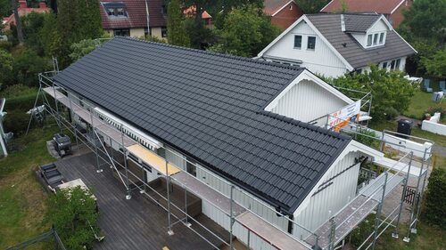 Vitt hus med nylagt svart tak i betongpannor, byggnadsställningar runt huset.
