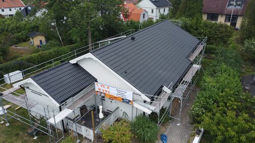 Vitt hus med byggnadsställningar och nylagt svart tak.