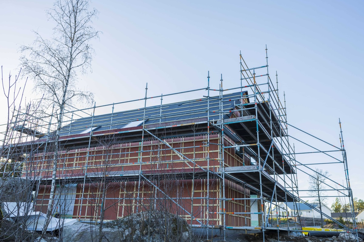 Hus under byggnation med byggställning runt fasaden mot blå himmel.