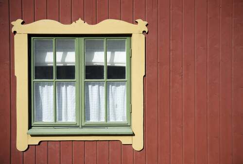 Fönster med gröna karmar och dekorativ gul foderlist på en faluröd träfasad.