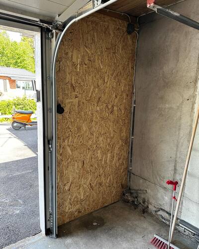 Insidan av ett garage med påbörjad isolering av port, träfiberskiva monterad på ena halvan.
