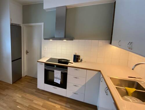 Modernt kök med vita luckor, kakel, spishäll och diskho, sett från sidan med bra överblick.