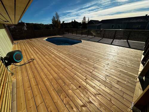 Stor altan i trä med inbyggd pool, solbelyst under klarblå himmel.