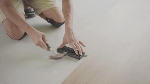 Närbild på hantverkare som lägger trägolv med verktyg