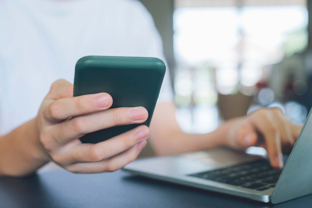 En person som håller en mobiltelefon framför en bärbar dator.