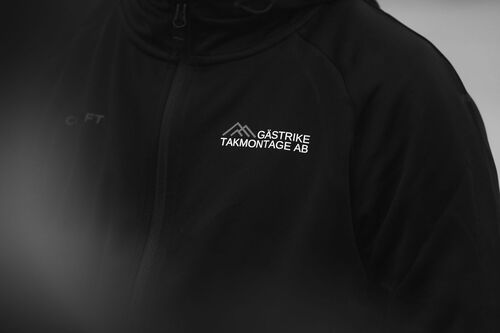 Närbild i svartvitt av jacka med logotypen Gästrike Takmontage AB.