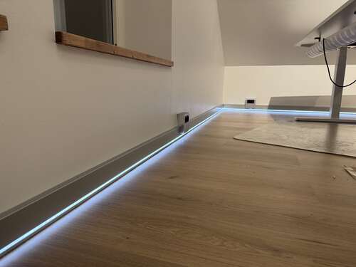 LED-list installerad längs golvsockel som skapar indirekt belysning i ett rum med trägolv.