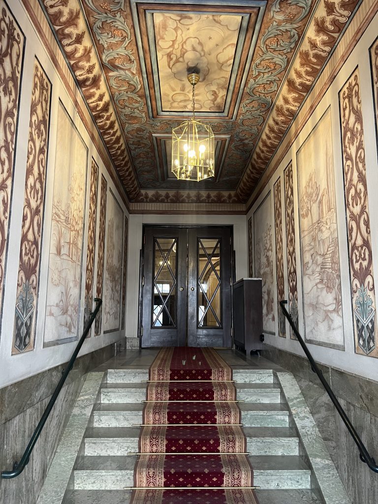 Dekorativt trapphus med väggmålningar, stentrappa och entrématta.